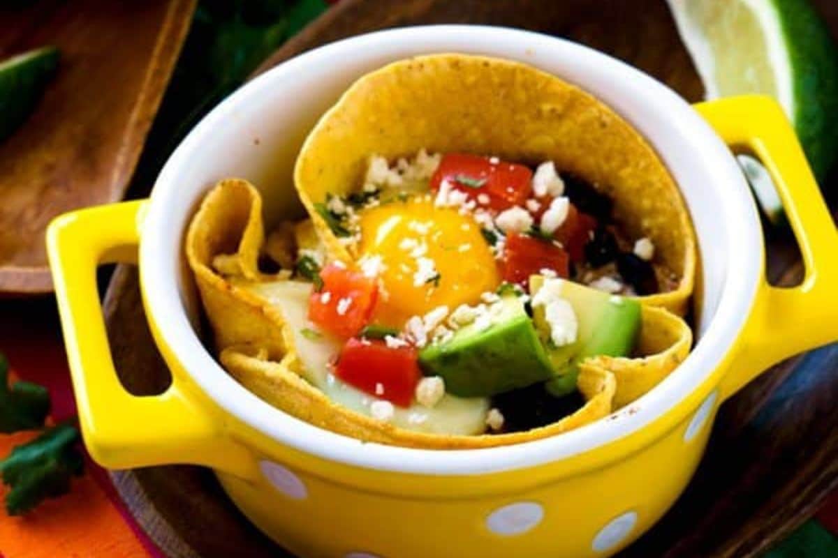 A tortilla cup filled with egg, avocado, tomato, cheese, and herbs in a yellow polka dot dish.
