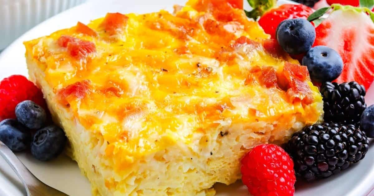A cheesy breakfast casserole with berries and a strawberry garnish on a white plate.