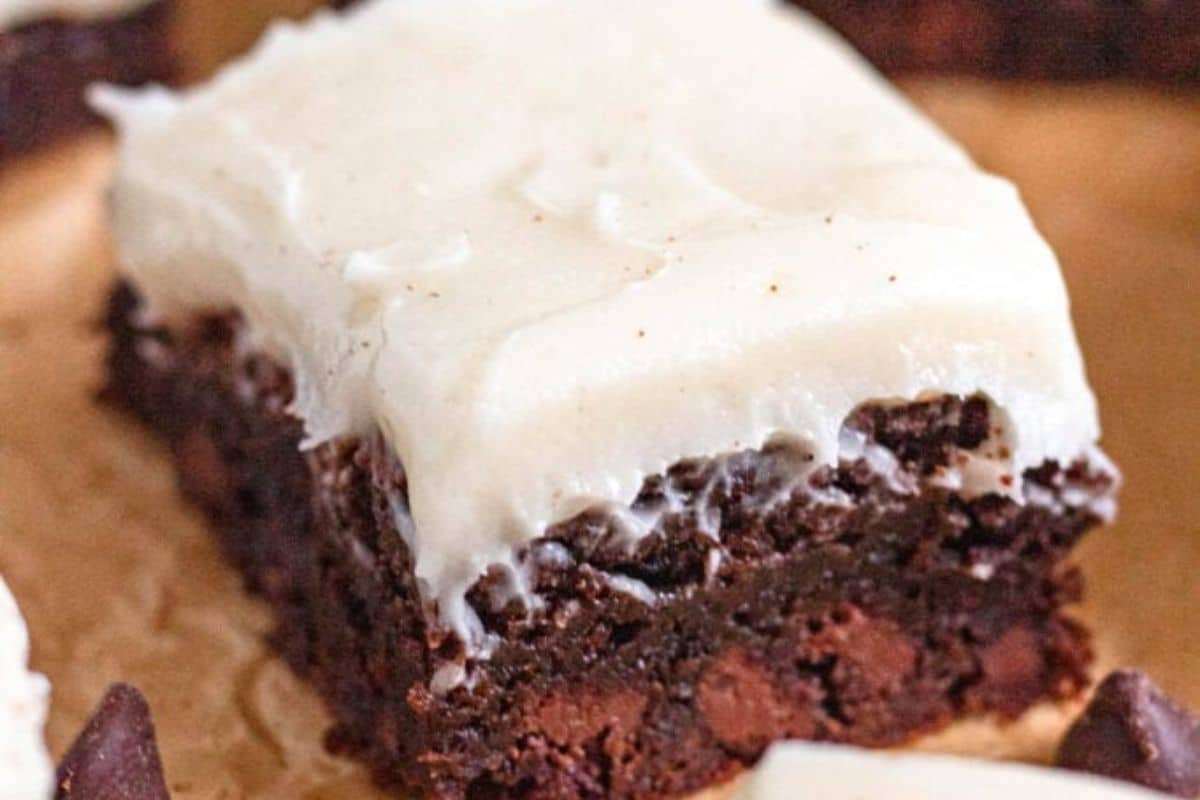 A frosted chocolate brownie topped with thick white icing, sitting on brown parchment paper.