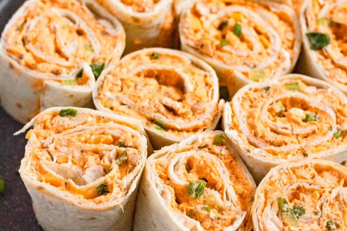 Close-up of tortilla pinwheels filled with a creamy orange spread and garnished with chopped green herbs.