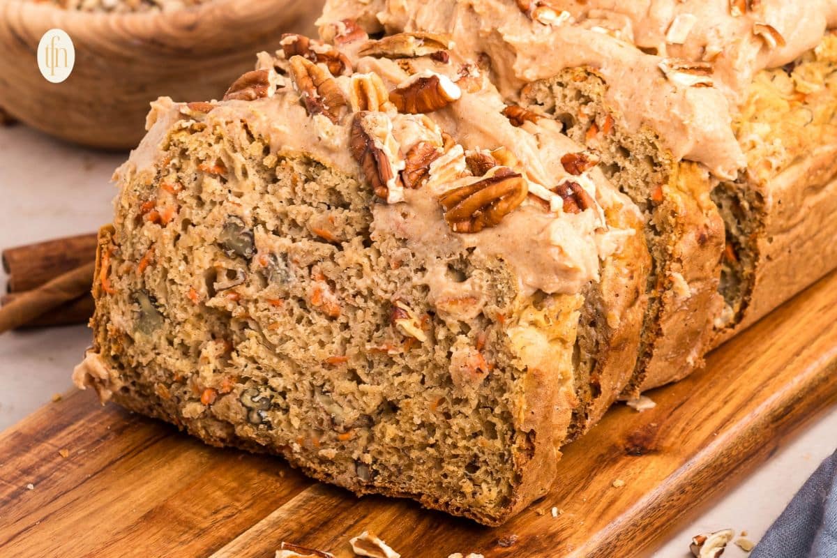 Sliced carrot bread with icing and pecans on a wooden board.