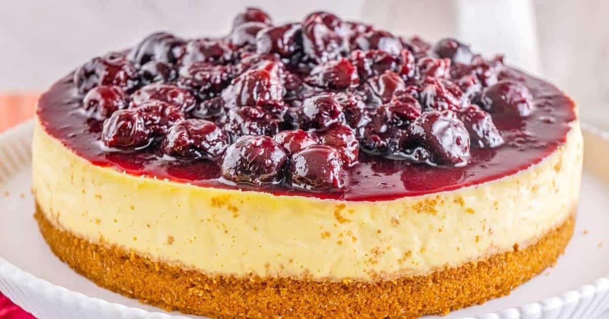 Cheesecake topped with glossy cherry sauce on a plate, featuring a golden graham cracker crust.