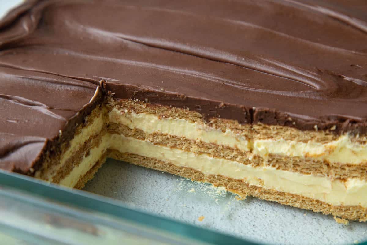 A layered dessert with chocolate topping and creamy filling in a glass dish, a large piece removed.