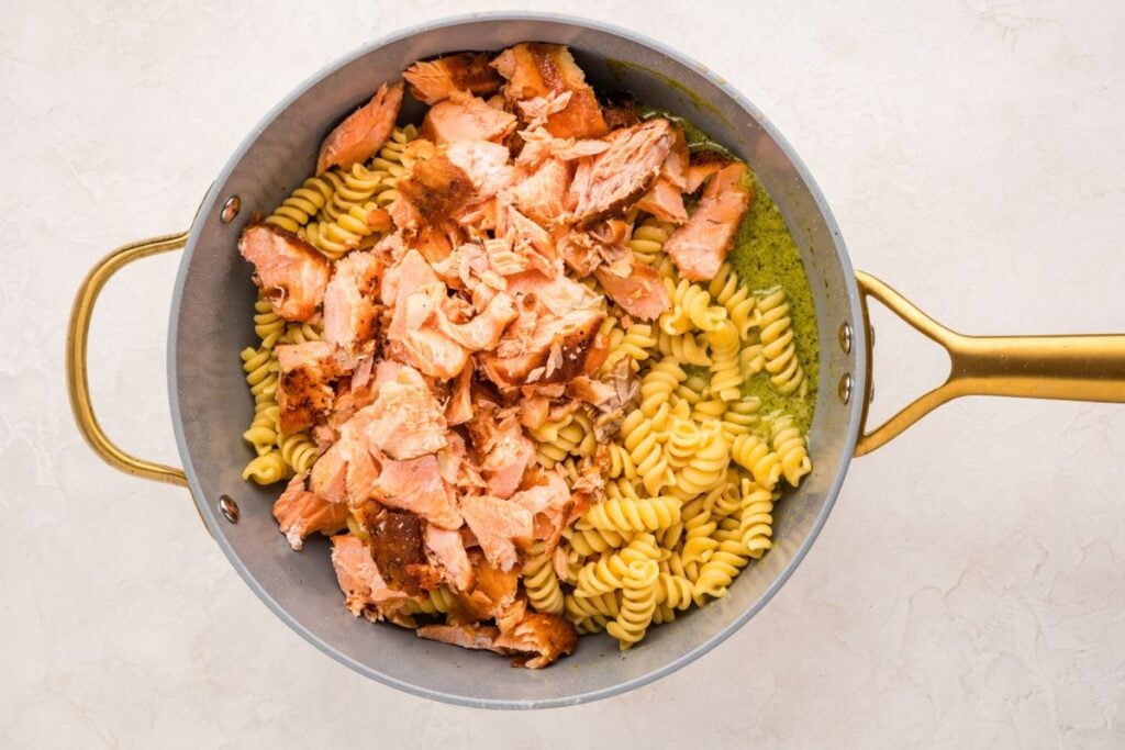 A pan with fusilli pasta and flaked cooked salmon on a light background.