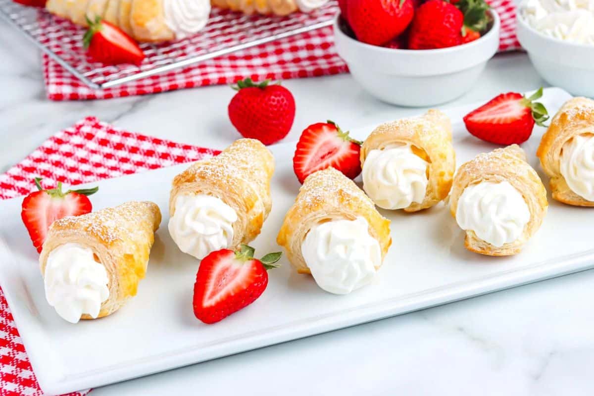 Cream horns filled with whipped cream on a white plate, garnished with fresh strawberries.