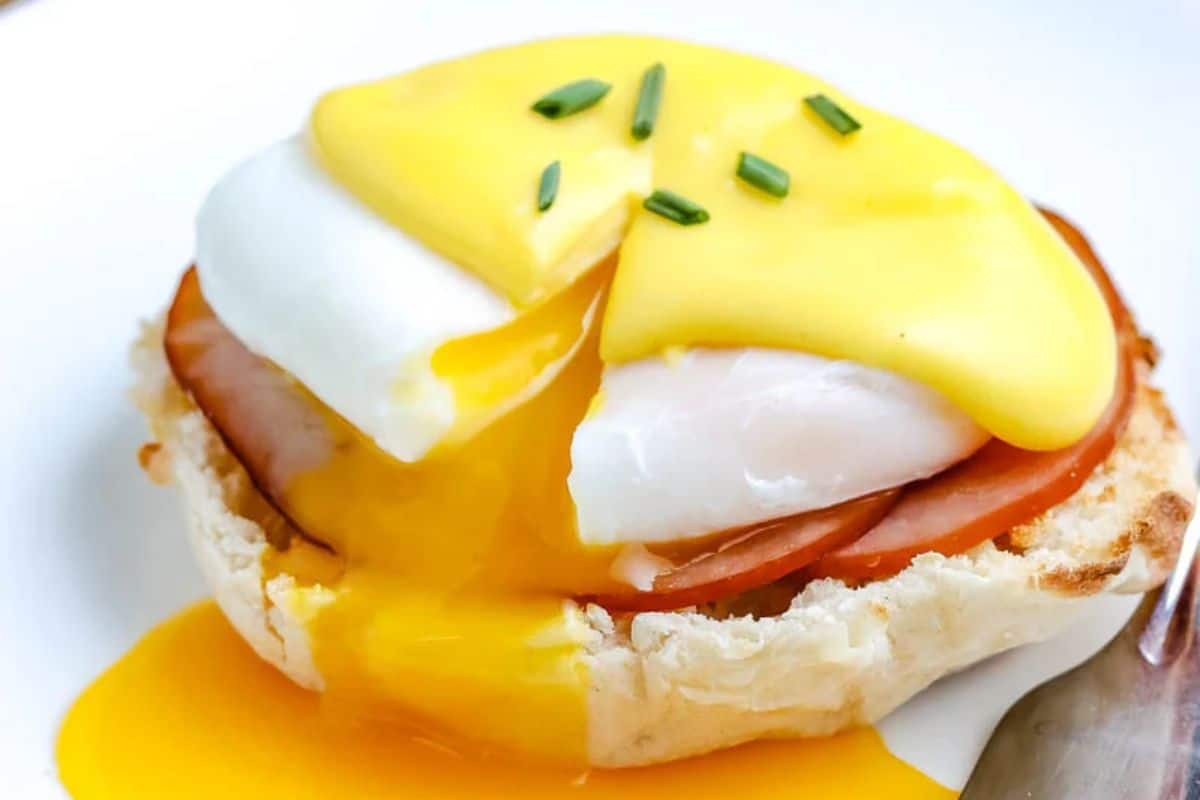 Eggs Benedict with runny yolk, ham, and hollandaise sauce on an English muffin, garnished with chives.