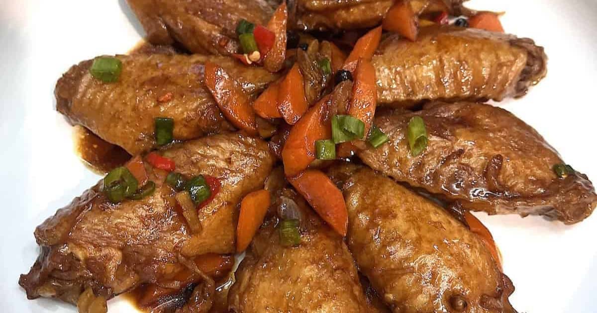 Braised chicken wings with sliced carrots, green onions, and sauce, arranged neatly on a white plate.