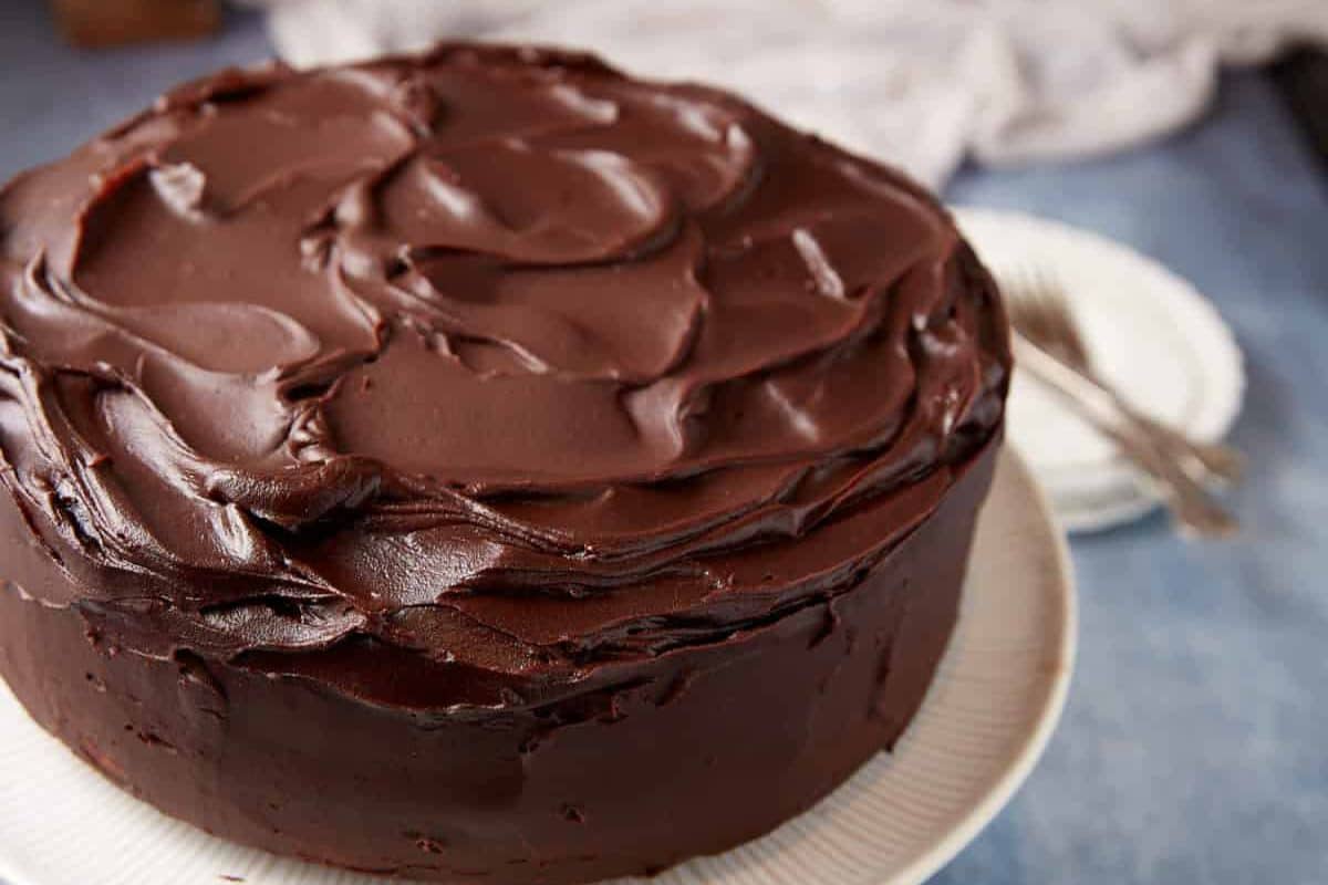 A round chocolate cake with rich, glossy chocolate frosting on a white plate.