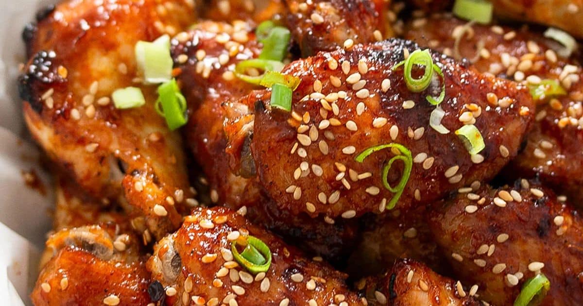 Close-up of glazed chicken wings topped with sesame seeds and sliced green onions.