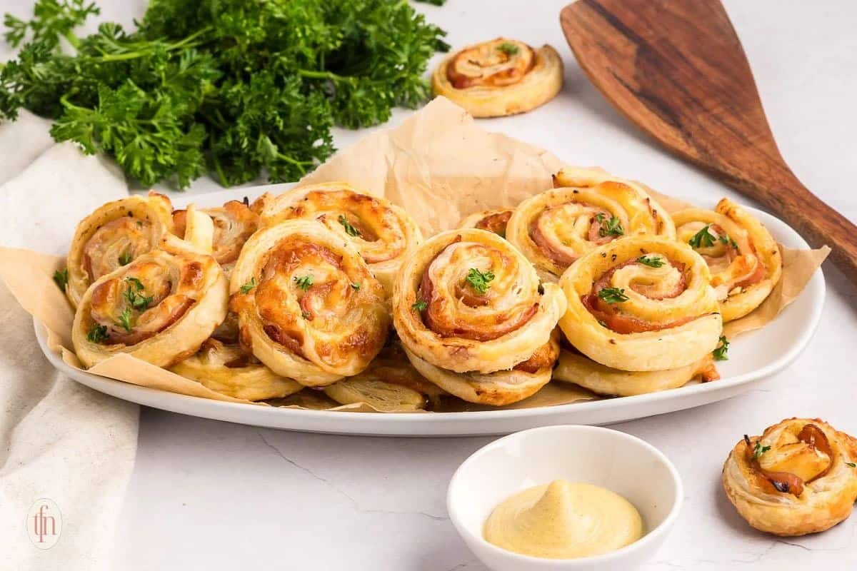 A plate of savory pastry pinwheels with herbs, served with dipping sauce and fresh parsley on the side.