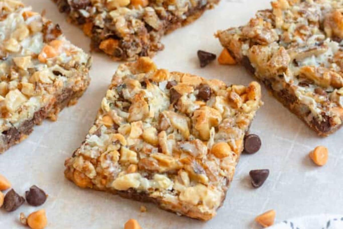 A close-up of a bar cookie with visible chocolate chips, butterscotch chips, nuts, and coconut.