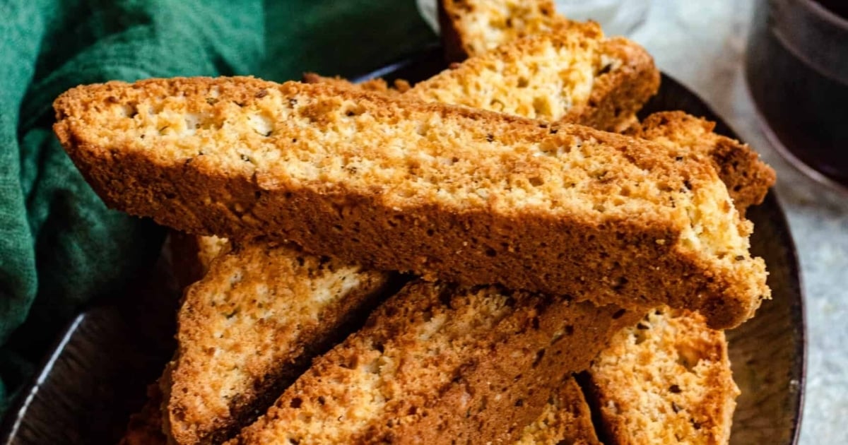 A close-up of several golden-brown biscotti stacked on a dark plate.