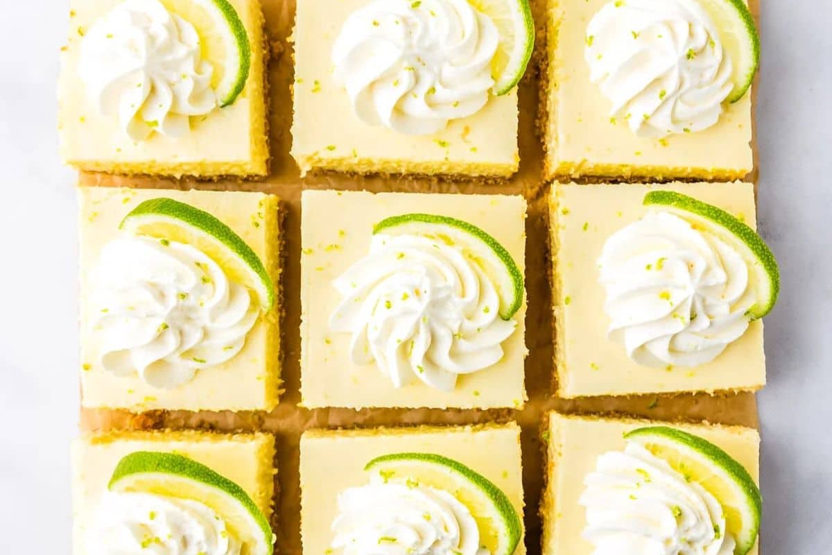 Nine key lime pie bars topped with whipped cream and lime slices, arranged neatly in a grid pattern.