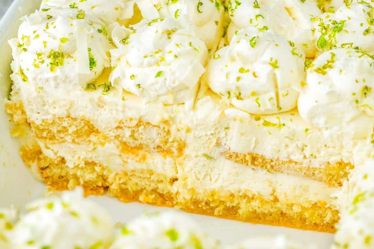 Close-up of a creamy, layered dessert topped with whipped cream, lime zest, and white chocolate shavings.