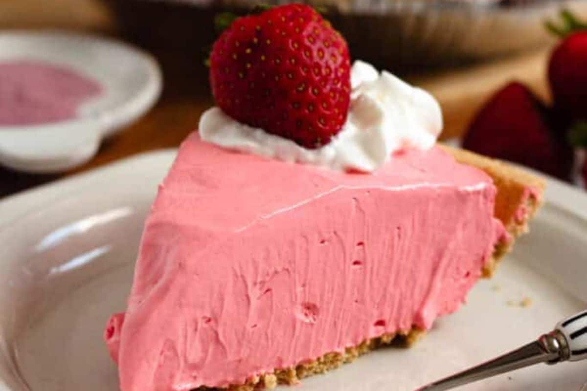 A slice of pink strawberry cream pie topped with whipped cream and a fresh strawberry on a plate.