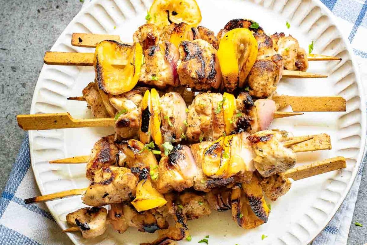 Grilled chicken and yellow bell pepper skewers on a white plate, garnished with herbs.