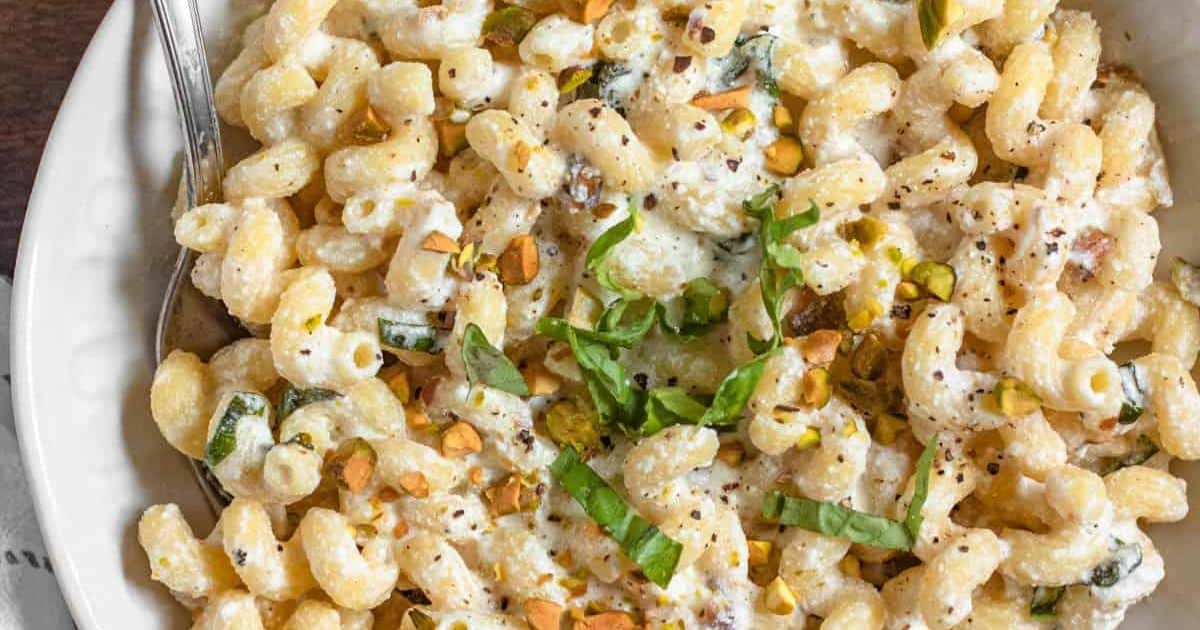 Creamy pasta with zucchini, pistachios, and basil in a white bowl with a fork.