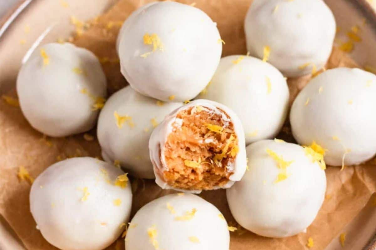 White chocolate-covered cake balls piled on parchment paper, one with a bite showing a moist, orange interior.