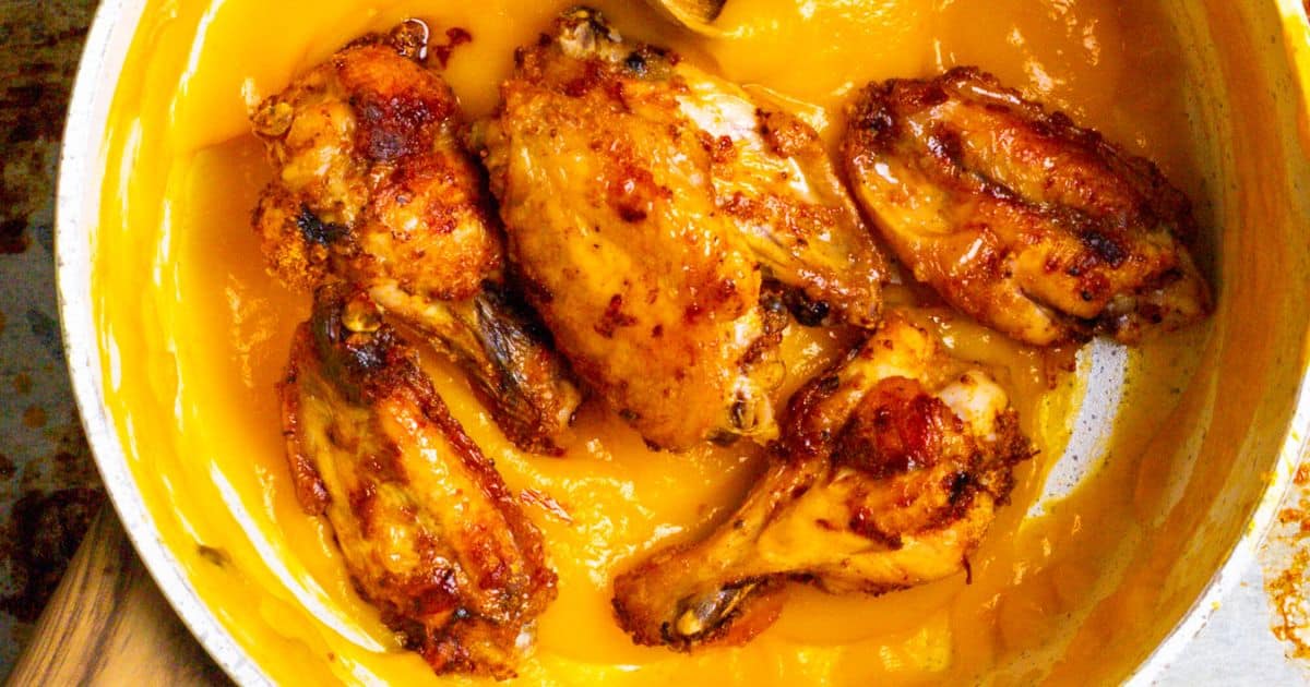 Chicken wings coated in a bright orange sauce in a white pan.