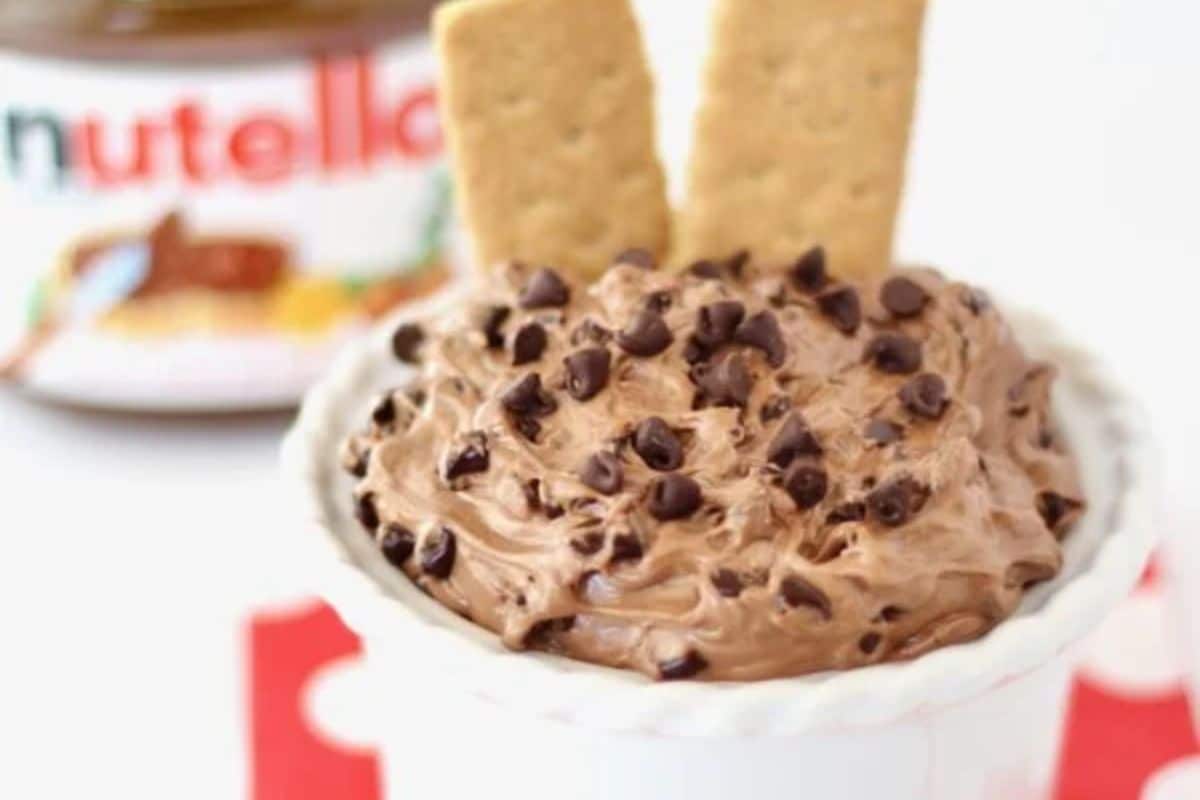 Chocolate chip dip with two graham crackers in a bowl; Nutella jar blurred in the background.