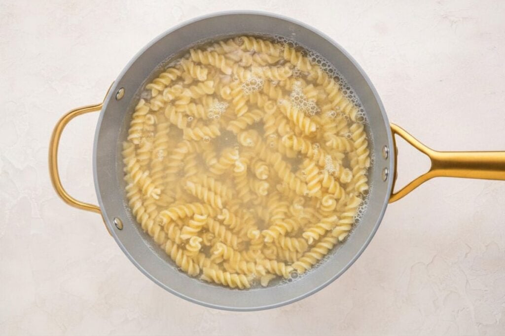 A pot of rotini pasta boiling in water on a light-colored surface.