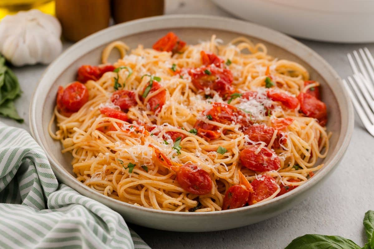 A bowl of spaghetti topped with tomato sauce, grated cheese, and chopped herbs, with a fork beside the bowl.