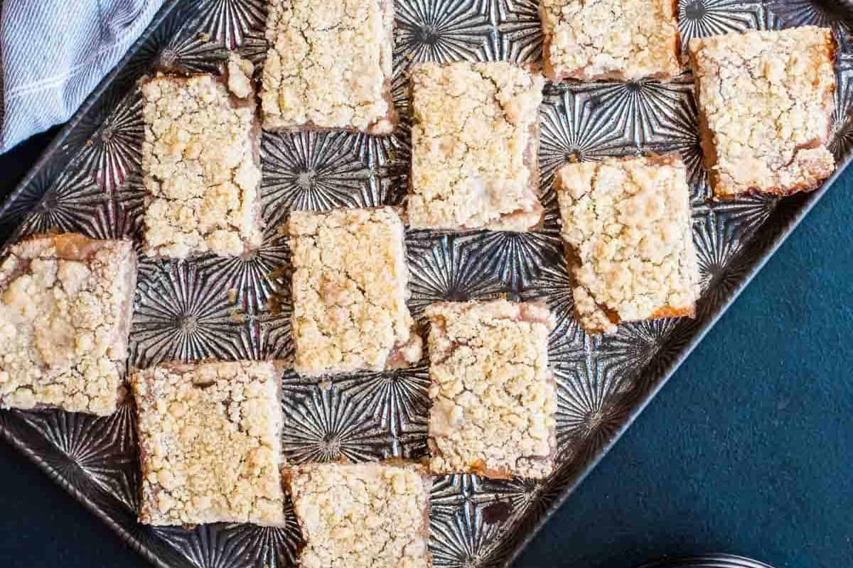 A tray of rectangular crumb-topped dessert bars arranged in rows on a patterned metal baking sheet.
