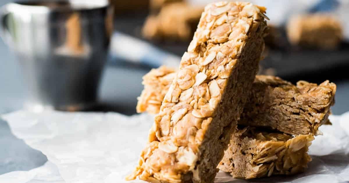 Three homemade granola bars stacked on parchment paper with a blurred cup in the background.