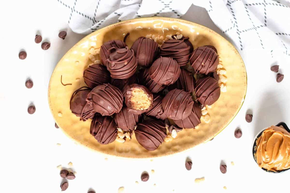A beige plate filled with chocolate-covered peanut butter balls, with one ball bitten to show the inside.