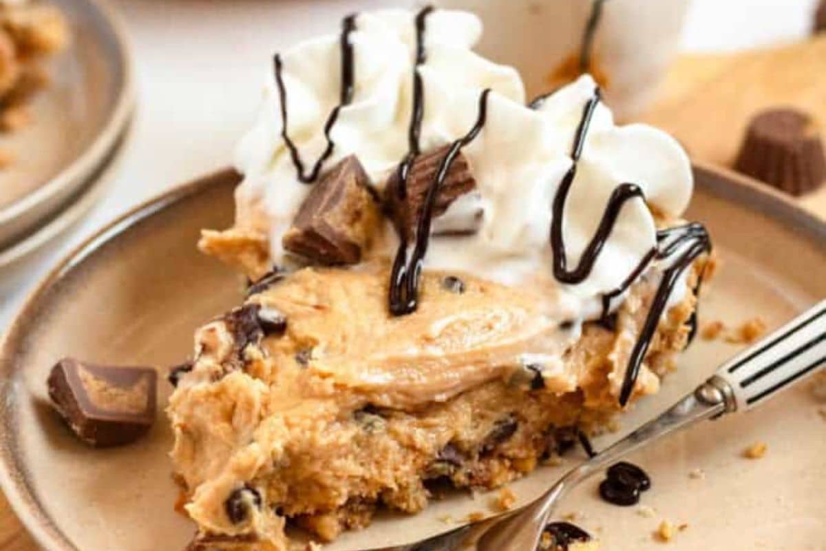 A slice of peanut butter pie topped with whipped cream, chocolate drizzle, and peanut butter cups on a plate.
