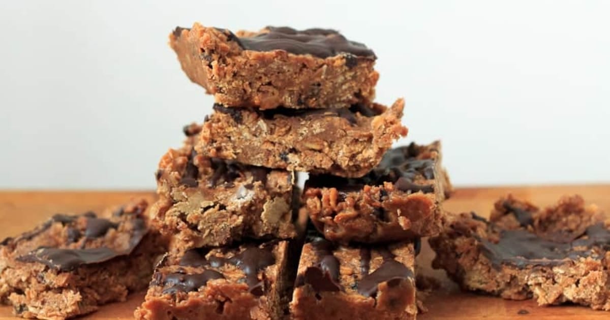 A stack of chocolate-drizzled granola bars arranged on a wooden surface against a plain background.