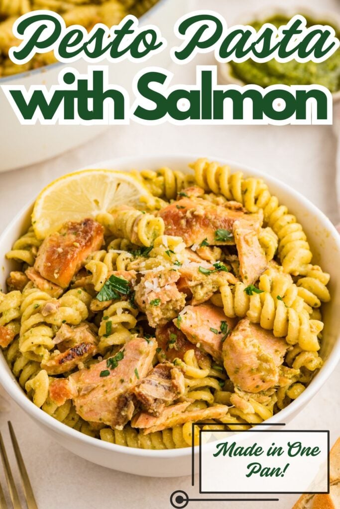 A bowl of rotini pasta with pesto sauce and salmon, topped with lemon slices and herbs. Text reads "Pesto Pasta with Salmon.