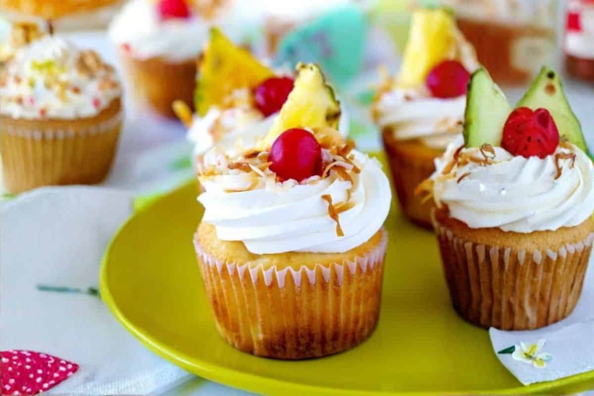Cupcakes with white frosting, fruit toppings, and sprinkles on a green plate.