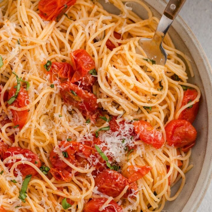 Spaghetti with cherry tomatoes, grated cheese, and fresh basil, with a fork twirling some pasta.