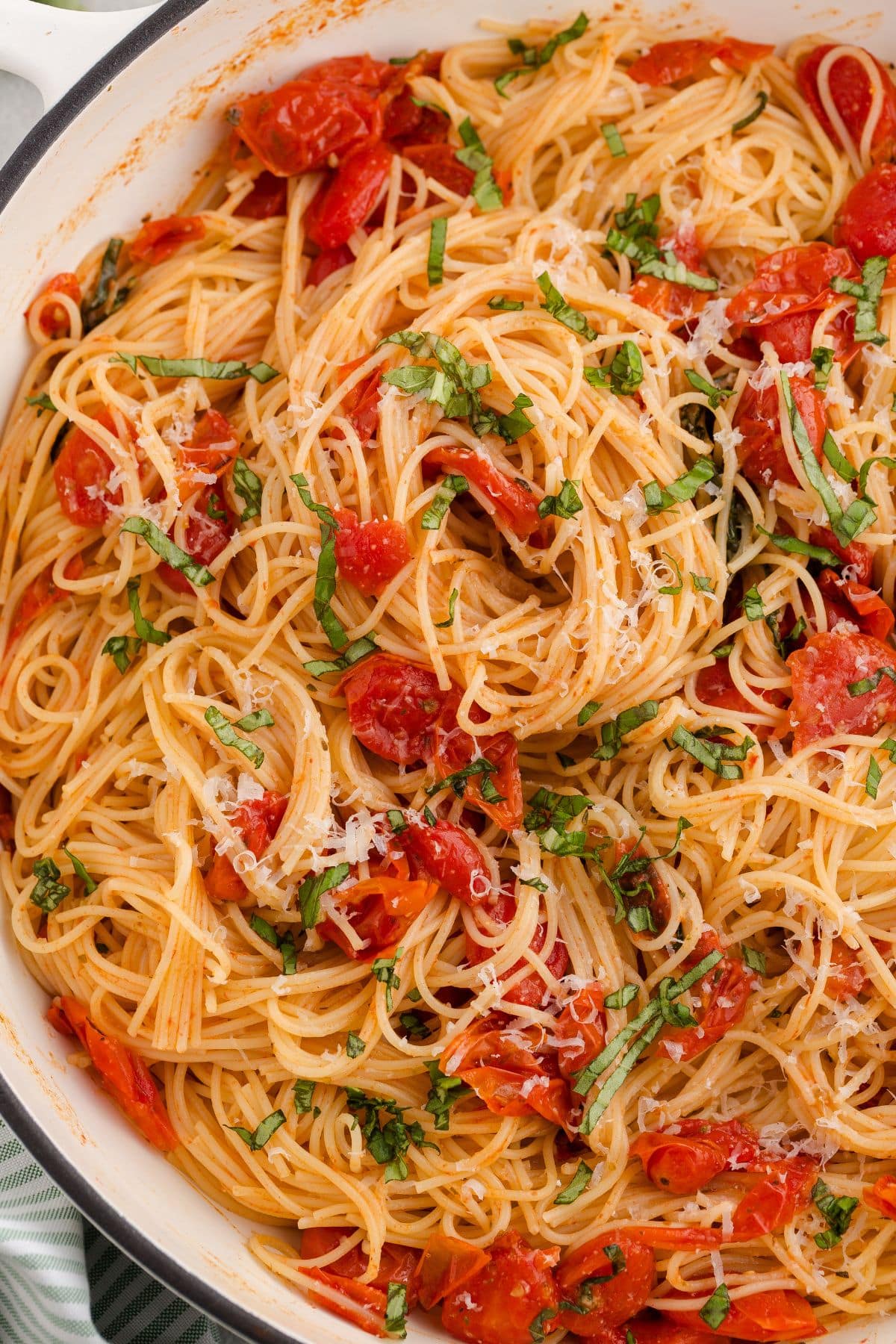 Spaghetti tossed with tomato sauce, fresh basil, and grated cheese in a white dish.