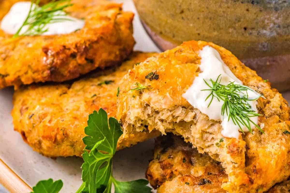 Golden salmon patties with a dollop of sour cream and dill, garnished with fresh parsley on a plate.