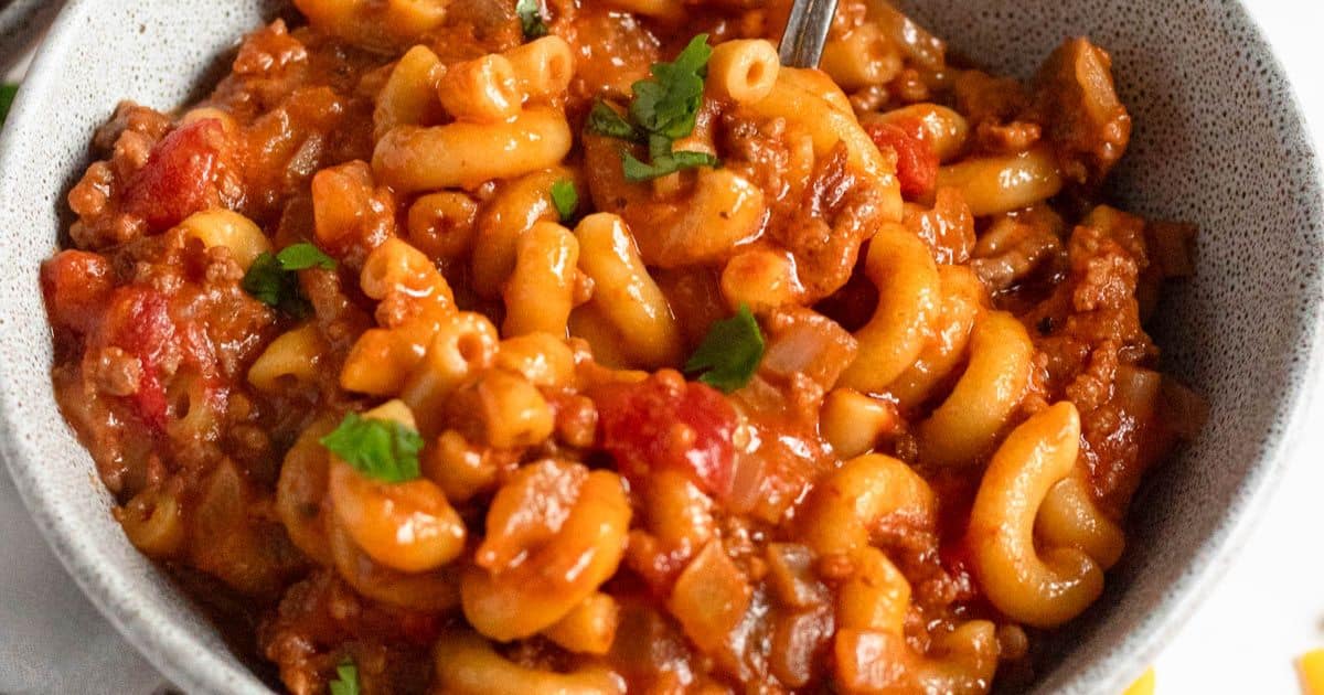 American goulash with macaroni, ground beef, and tomatoes in a bowl, garnished with parsley.