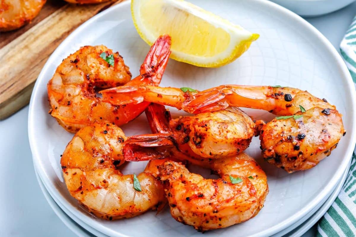 Four seasoned grilled shrimp with a lemon wedge on a white plate.