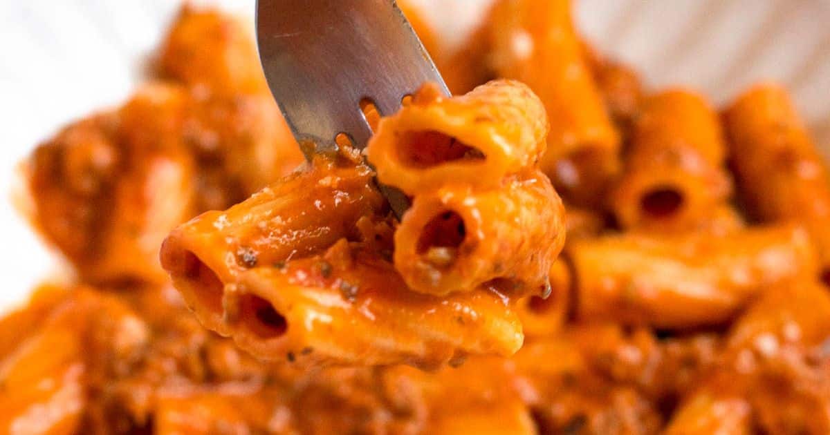 A fork lifts a portion of pasta covered in a creamy, orange sauce.