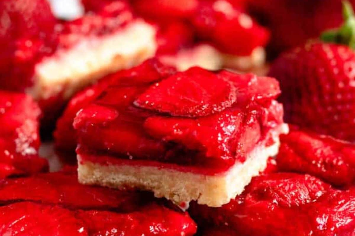 A close-up of a strawberry dessert bar with a shortbread crust and fresh strawberry topping.