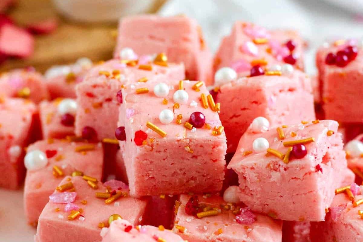 Close-up of pink fudge squares topped with colorful sprinkles and candy pearls.