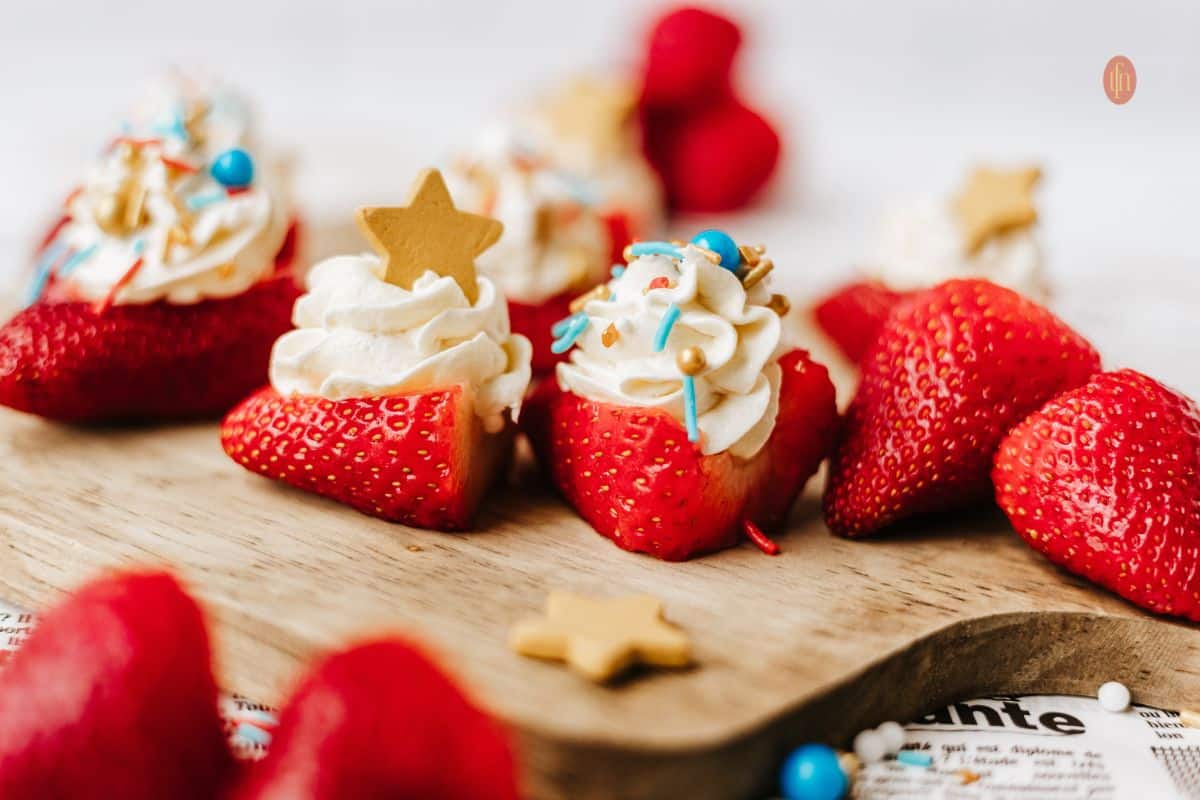Fresh strawberries topped with whipped cream, sprinkles, and gold star decorations on a wooden board.