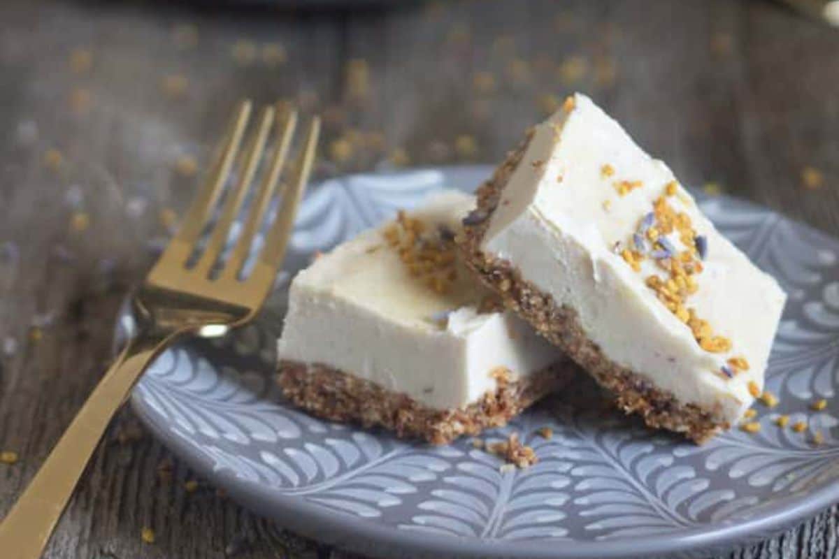 Two cheesecake bars with crumb crust and sprinkled topping, served on a patterned plate with a gold fork.