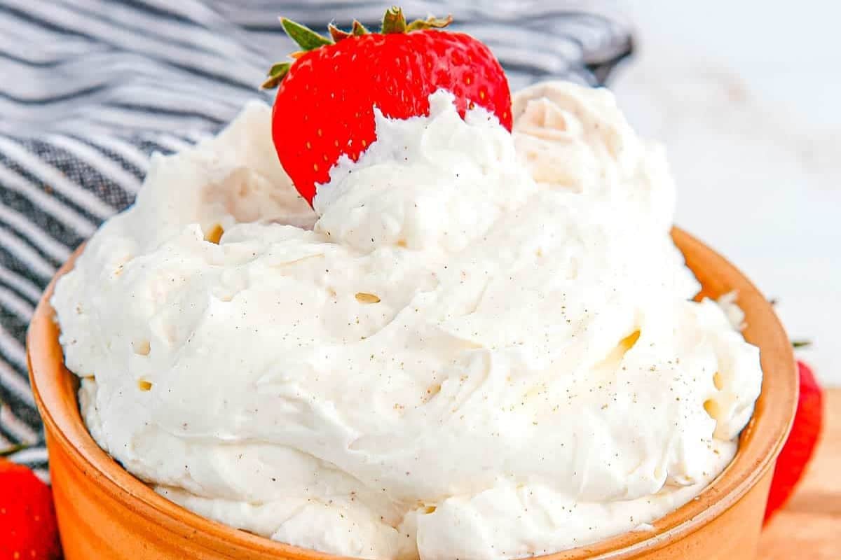 A bowl of fluffy whipped cream topped with a fresh strawberry, with a striped cloth in the background.