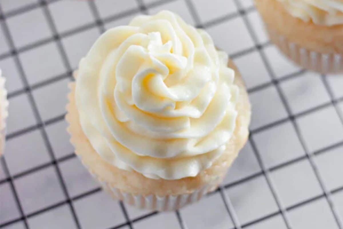 Vanilla cupcake with swirled white frosting on a wire cooling rack.