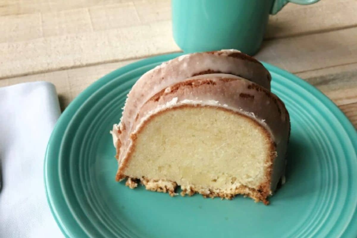 A slice of glazed bundt cake on a turquoise plate next to a matching mug and a white napkin.