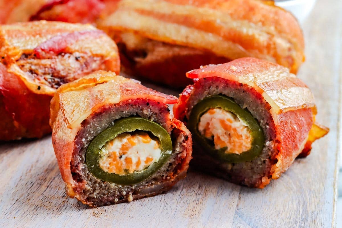 Bacon-wrapped jalapeño poppers stuffed with cream cheese, sliced open on a wooden board.