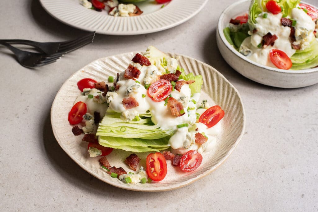 Wedge salad with bacon, cherry tomatoes, blue cheese, and dressing on a plate, with a fork nearby.