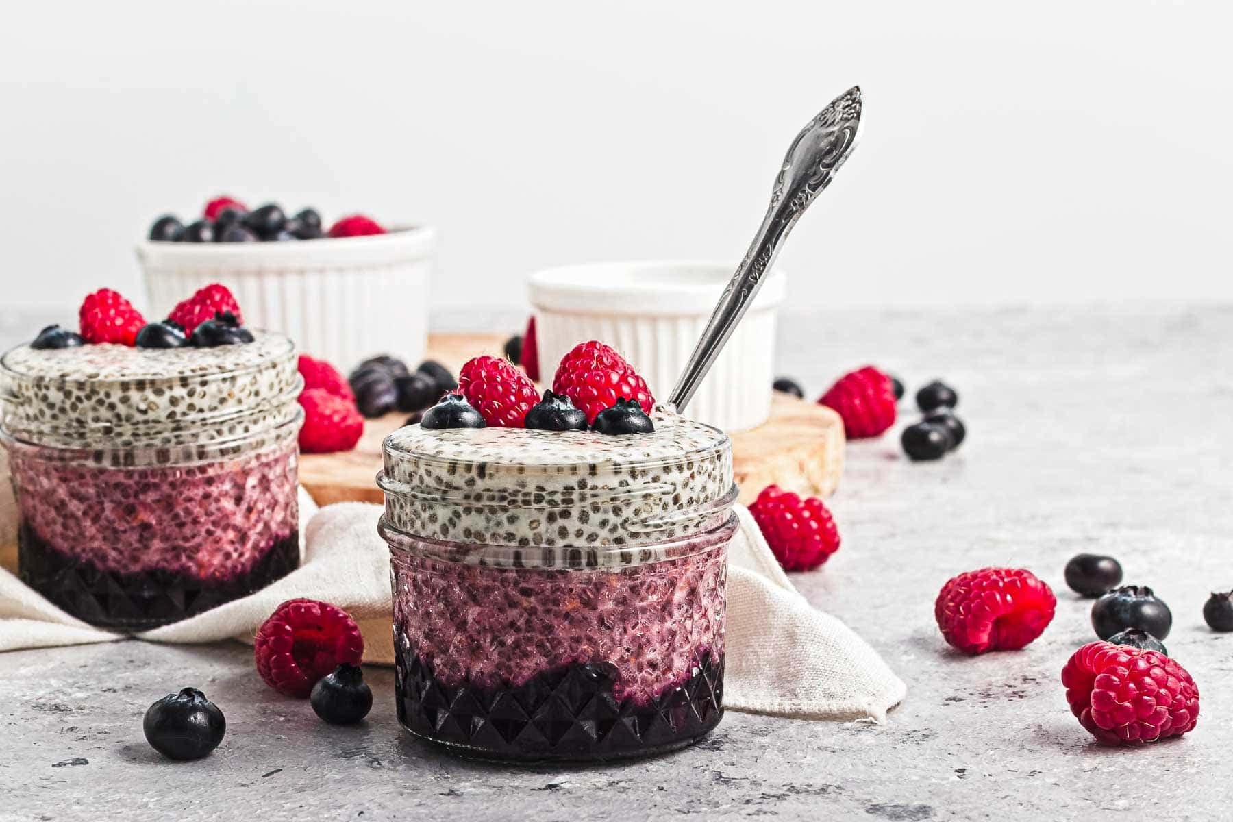 Glass jars filled with layered chia pudding and berries, with a spoon and fresh berries scattered around.