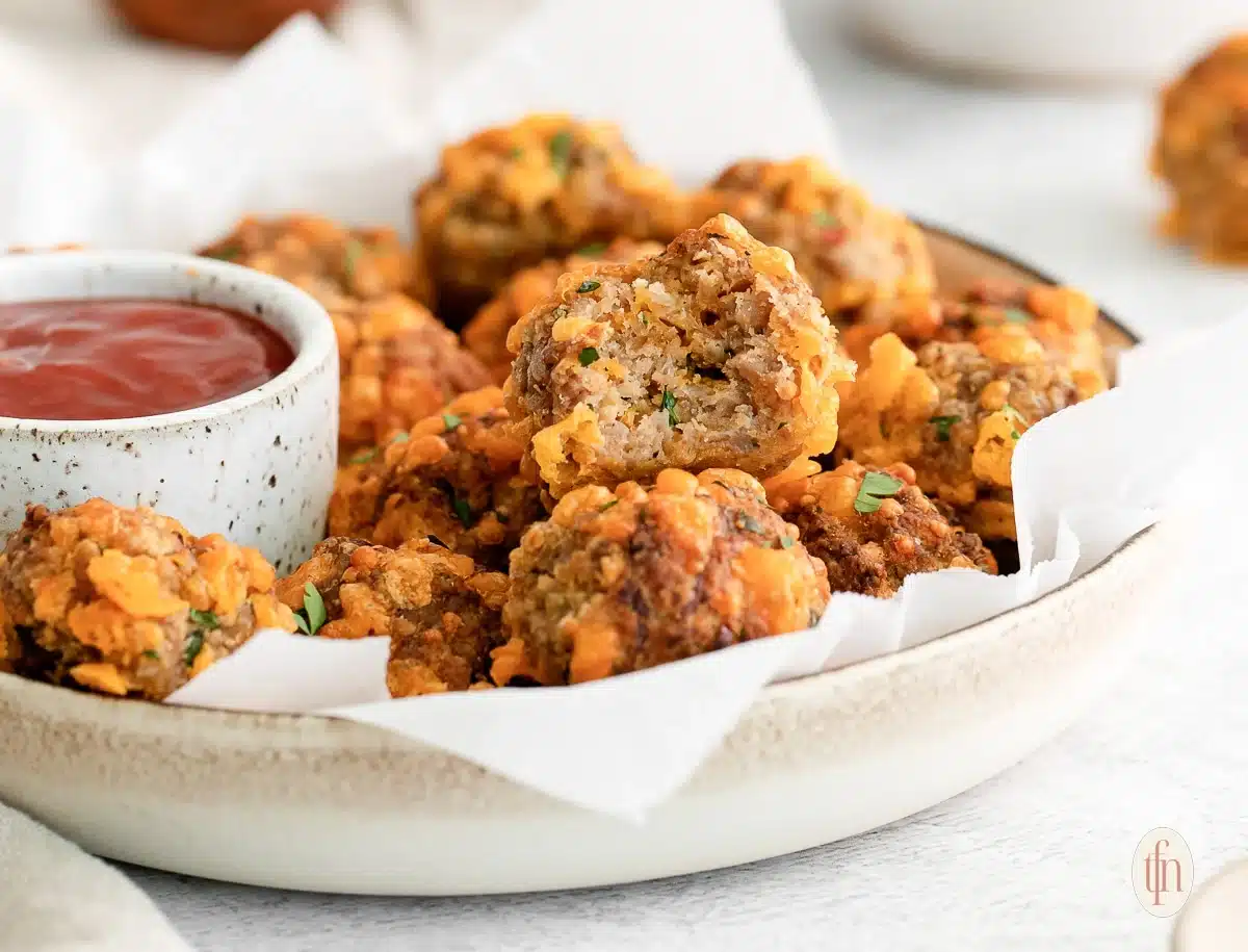 A plate of sausage balls with a dipping sauce, one ball is bitten to show the inside.